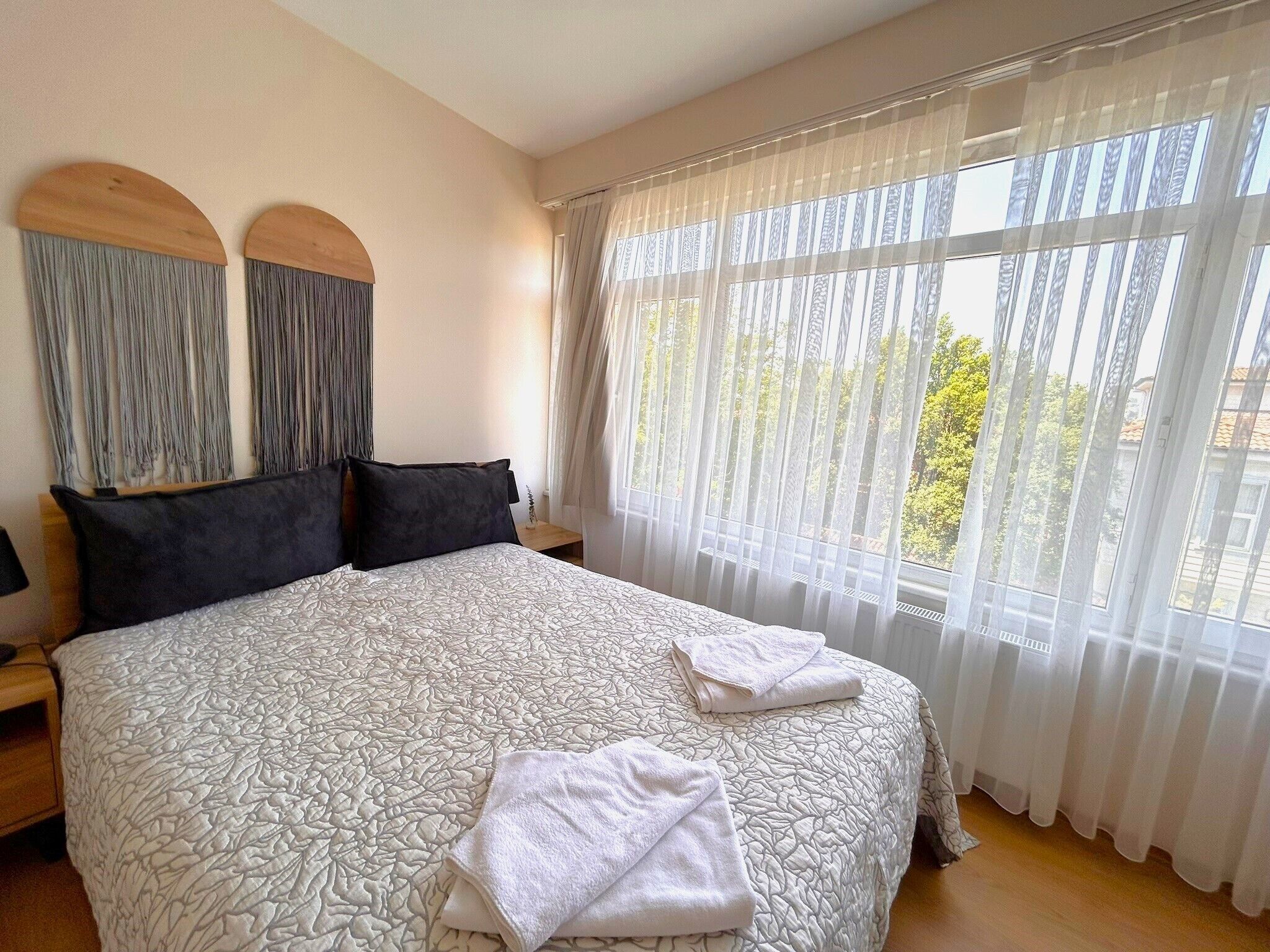 Een net opgemaakt bed met een bedovertrek met patroon, twee zwarte kussens en een paar opgevouwen handdoeken op het bed.