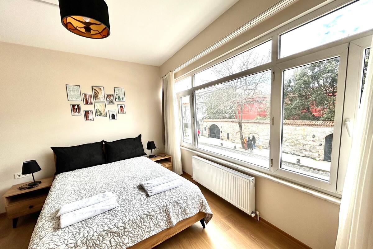 Une chambre avec un grand lit, une fenêtre donnant sur une cour et des œuvres d’art accrochées au mur.