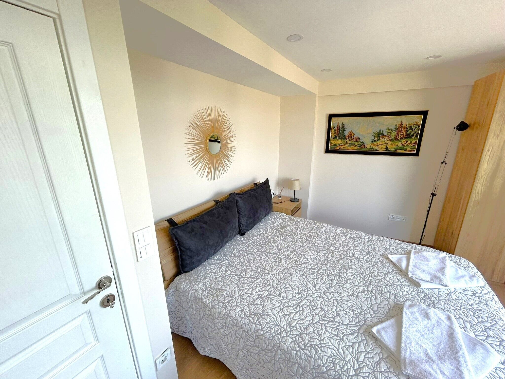 A bedroom with a bed, a nightstand, a lamp, a painting, and a door.
