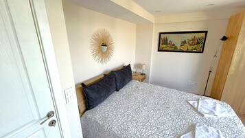 A bedroom with a bed, a nightstand, a lamp, a painting, and a door.