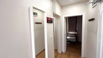 A hallway with a wooden floor, white walls, and a door leading to a room with a bed and a window.