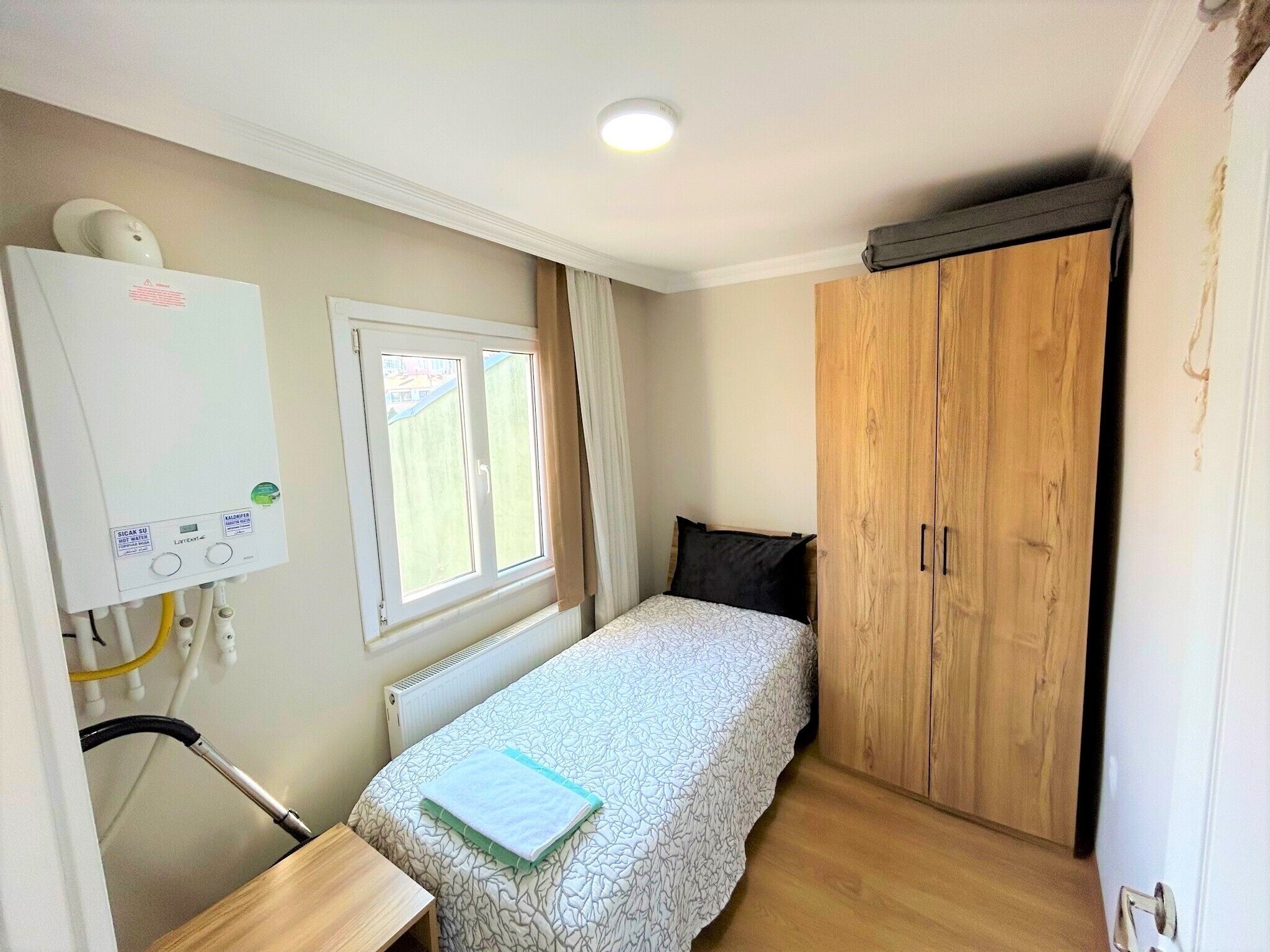 Un dormitorio con una cama, un armario de madera, un radiador, una ventana con cortinas y una pizarra en la pared.