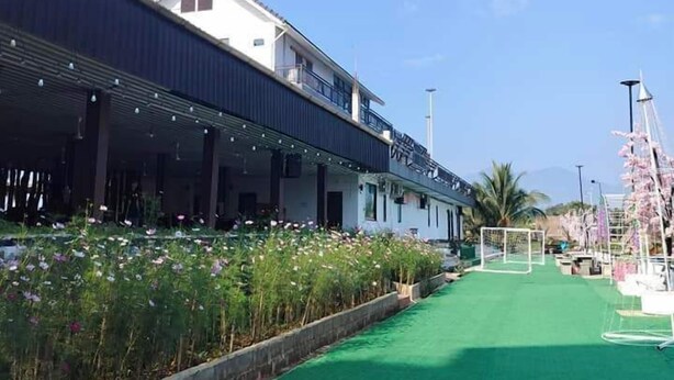 A building with a covered outdoor area, a green artificial turf path, and a flower garden. - Coconut Garden Garden Cafe (Mae Sai)