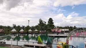 A large outdoor pool with a water slide, surrounded by palm trees and a few small huts. - Coconut Garden Garden Cafe (Mae Sai)