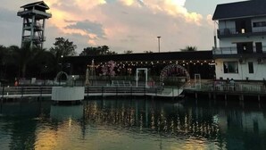 A waterfront area with a tower, a building with a balcony, and a reflection in the water. - Coconut Garden Garden Cafe (Mae Sai)