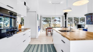 Una cocina moderna con armarios blancos, encimera de madera y un amplio ventanal con vistas a un paisaje exterior.