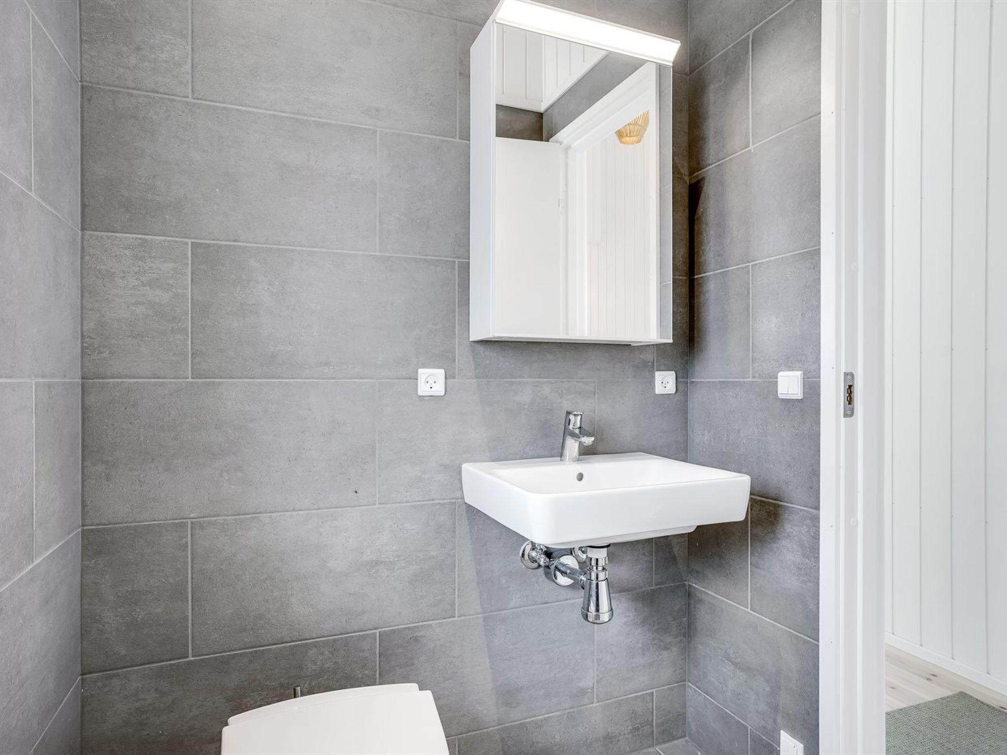 A bathroom with grey tiles, a white sink, and a mirror.