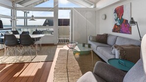 Un vaste espace de vie avec un balcon, une table à manger avec des chaises, un canapé et un tableau accroché au mur.
