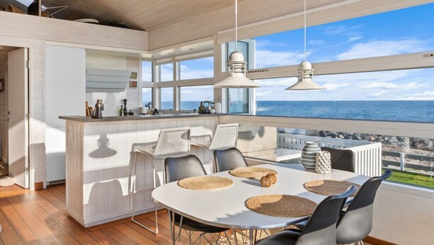 Une cuisine moderne dotée d’un grand îlot central, de meubles blancs et offrant une vue sur la mer.