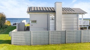 Une maison située sur la côte, avec une façade grise, une cheminée et un balcon.