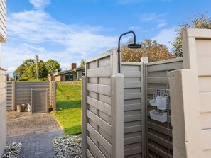Un espace extérieur clos, délimité par une clôture en bois, une porte en métal et un petit coffret blanc pour les installations techniques.