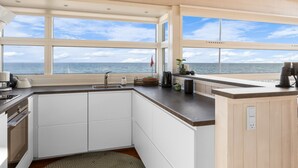Une cuisine moderne avec des meubles blancs, un plan de travail foncé et une grande fenêtre donnant sur la mer.
