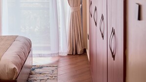A bedroom with a bed, a wardrobe, and a window with sheer curtains. - Sand Grains Residences 007 (Entebbe)
