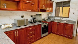 A kitchen with wooden cabinets, a microwave, a stove, and a sink. - Sand Grains Residences 007 (Entebbe)