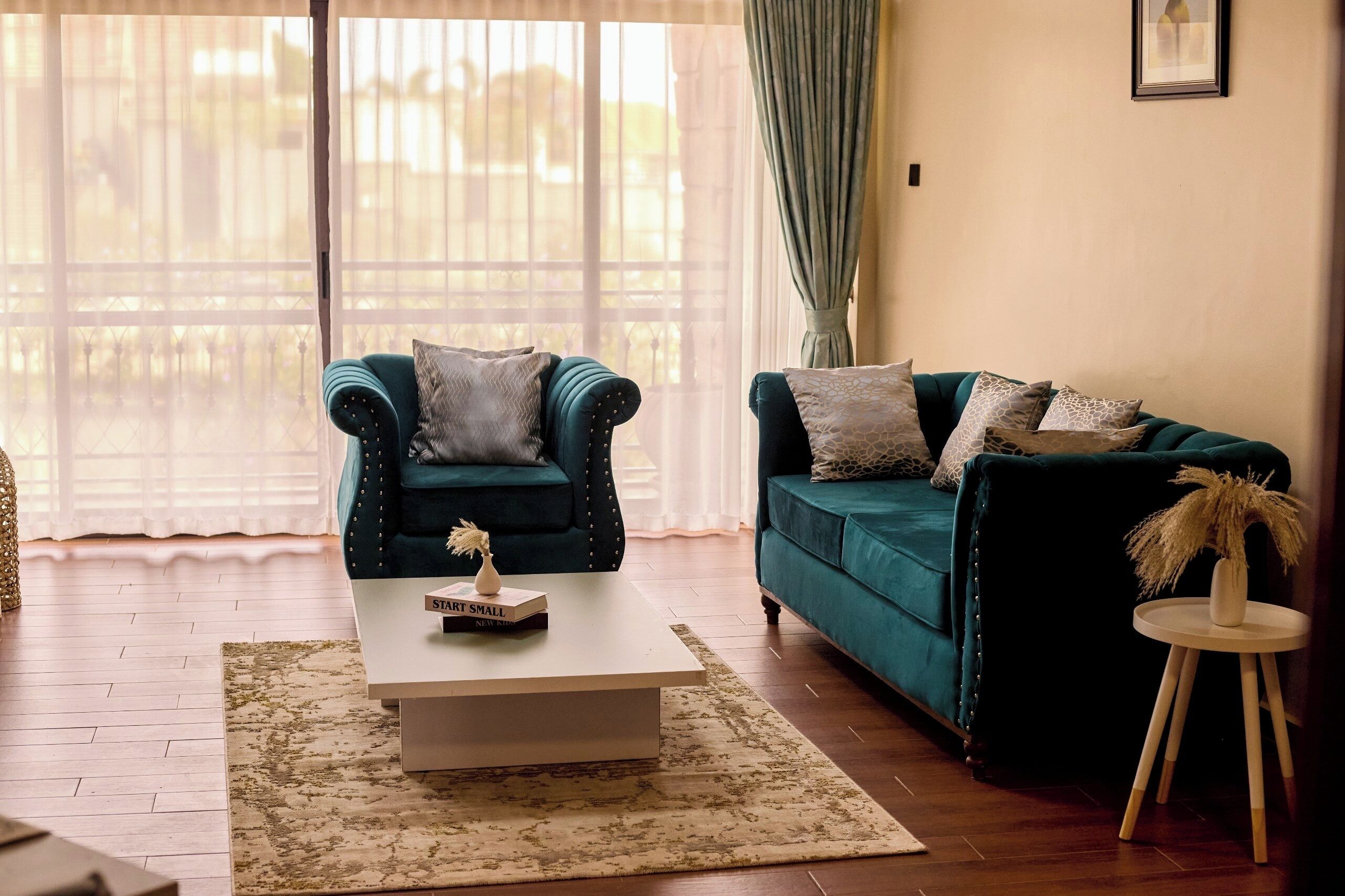 A living room with two teal sofas, a white coffee table, and a small side table with a vase.