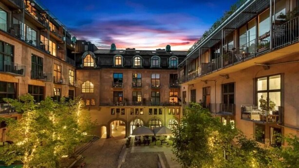 Un patio con un arco central, rodeado de edificios con balcones y zonas de estar al aire libre.