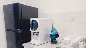Een kleine keuken met een zwarte koelkast, een witte magnetron en een blauwe lamp op het aanrecht.