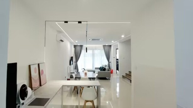 Een moderne woonkamer met een glazen scheidingswand, een eethoek en een keuken op de achtergrond.