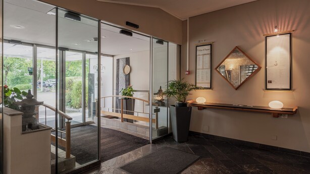 Un vestíbulo de hotel moderno con puertas de vidrio que dan a una escalera, una recepción y un espejo adosado a la pared.