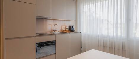 Una cocina moderna con electrodomésticos integrados, un ventanal con cortinas ligeras y un diseño minimalista.