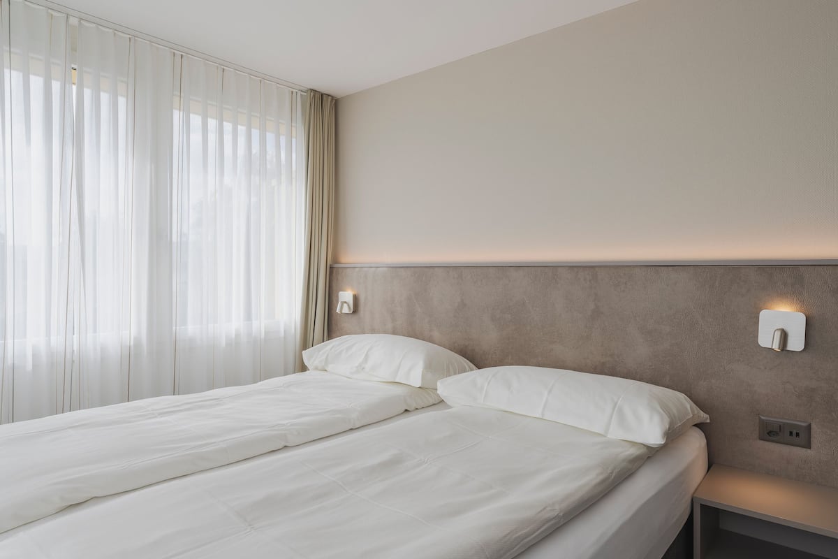 Una habitación de hotel moderna con una cama grande, una mesita de noche y una lámpara fijada a la pared.