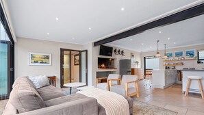 Ein modernes Wohnzimmer mit einer Couch, Sesseln, einem Kamin und einer Küchenzeile mit Esstisch und Bar.