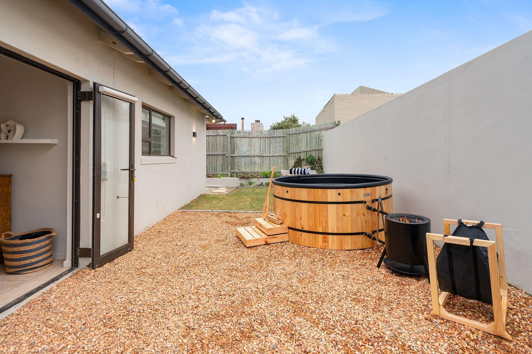 A backyard with a wooden barrel, a black trash can, and a wooden rack.