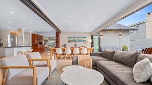 Ein modernes Wohnzimmer mit einer Couch, Stühlen, einem Esstisch und einer Küche im Hintergrund.