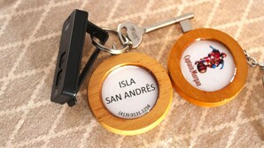 Two keychains with engraved text and a small image, placed on a patterned fabric background. - Pousada Captain Morgan (Pontal do Parana)