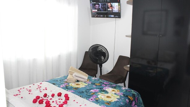 A hotel room with a bed, a TV mounted on the wall, a fan, and a chair. - Pousada Captain Morgan (Pontal do Parana)