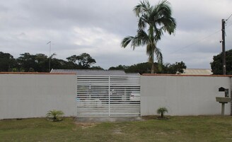 Un área cercada con una reja metálica, una palmera y una pared blanca.