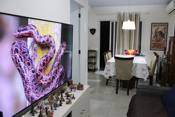 Ein Essbereich mit einem Tisch für zwei Personen, einem Fernseher, der ein farbenfrohes Bild zeigt, und einer Kristallleuchter.