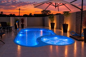 A swimming pool with a hot tub, surrounded by chairs and potted plants, under a large umbrella. - Pousada Captain Morgan (Pontal do Parana)