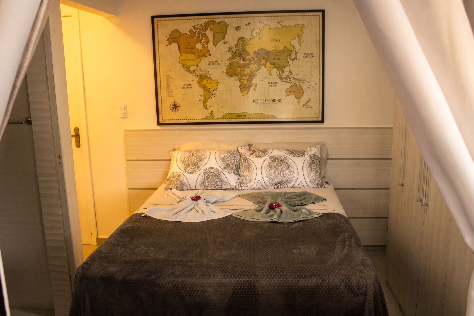 A bedroom with a bed, pillows, a map on the wall, and a door.