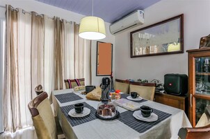 Un comedor con una mesa lista para dos, una cafetera y un armario con cristalería.