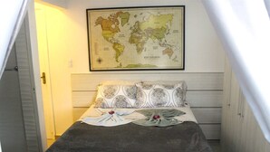 A small, cozy room with a bed, a world map on the wall, and a door leading to another room. - Pousada Captain Morgan (Pontal do Parana)