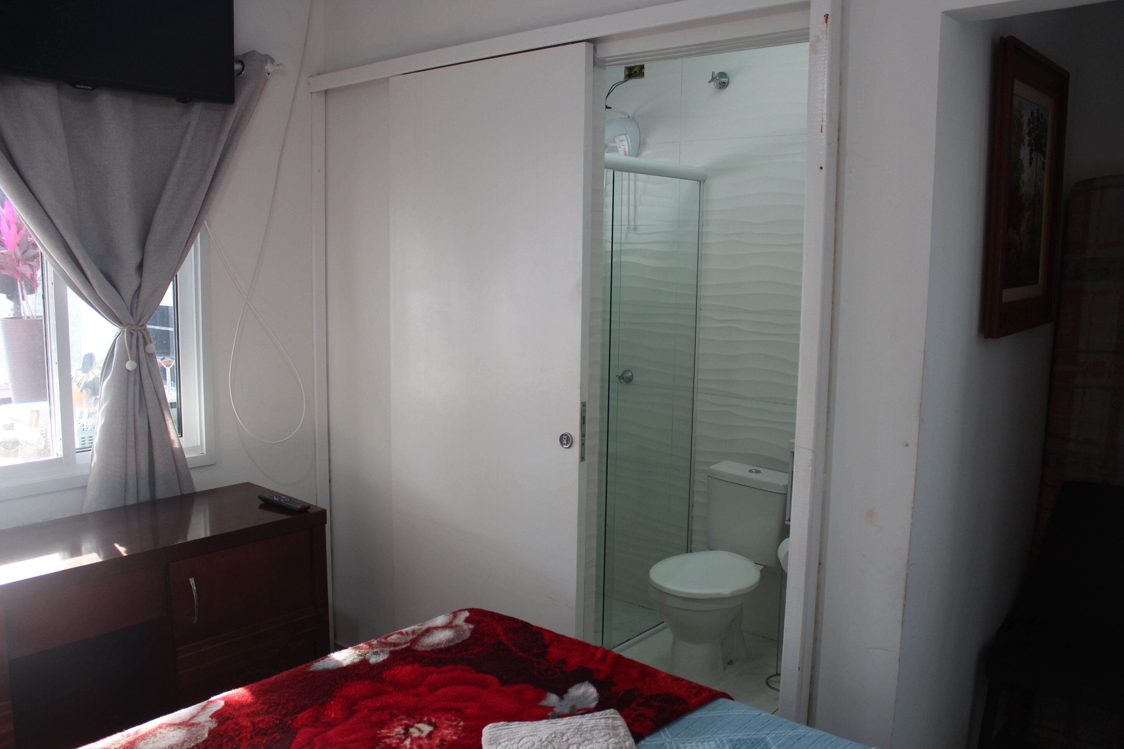 A bedroom with a bed, a dresser, a glass-enclosed shower, and a toilet.