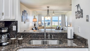 A kitchen with granite countertops, a double sink, and a coffee maker. There is a dining area with a view of the ocean. - Pier Point 57 (St. Augustine)