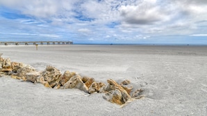 A beach with a rocky outcrop in the foreground and a pier extending into the water in the background. - Pier Point 57 (St. Augustine)