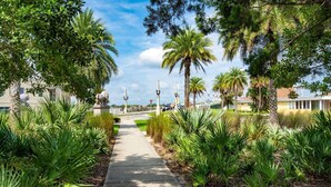A pathway lined with palm trees and other greenery, leading towards a building with a modern architectural style. - Pier Point 57 (St. Augustine)