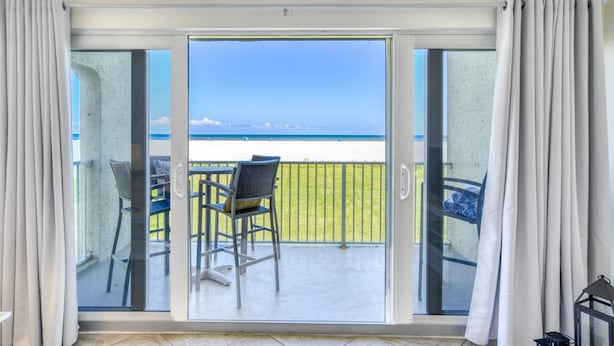 A balcony with a view of the beach, a chair, and a table. - Pier Point 57 (St. Augustine)