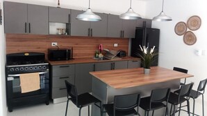 A modern kitchen with grey cabinets, a wooden countertop, a black stove, and a dining area with a wooden table and black chairs.
