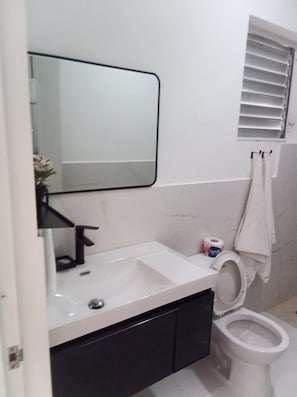 Ein Badezimmer mit einem weißen Waschbecken, einem Spiegel, einer Toilette und einem Handtuch an der Wand.