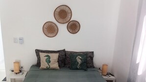 A neatly made bed with a green bedspread, two pillows with seahorse designs, and three woven wall decorations.