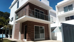 A modern two-story house with a balcony, large windows, and a concrete driveway.