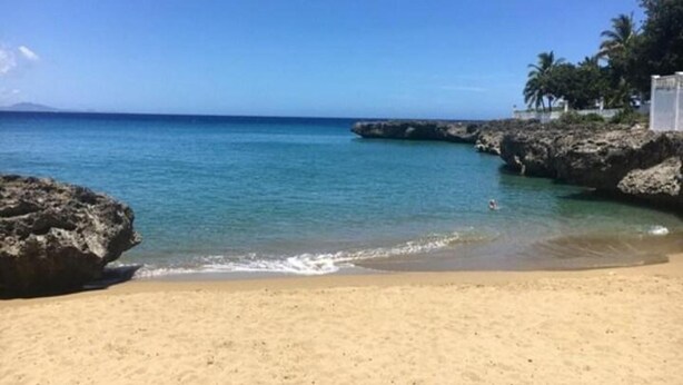 A sandy beach with clear blue water, rocky formations, and palm trees. - Tropical Paradise Villa in Sosua (Sosúa)