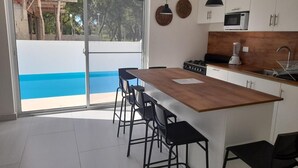 A modern kitchen with a wooden island, black bar stools, and a view of a blue pool through a sliding glass door. - Tropical Paradise Villa in Sosua (Sosúa)