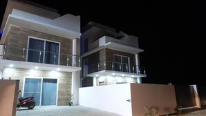A modern two-story house with a garage, a balcony, and a well-lit entrance. - Tropical Paradise Villa in Sosua (Sosúa)