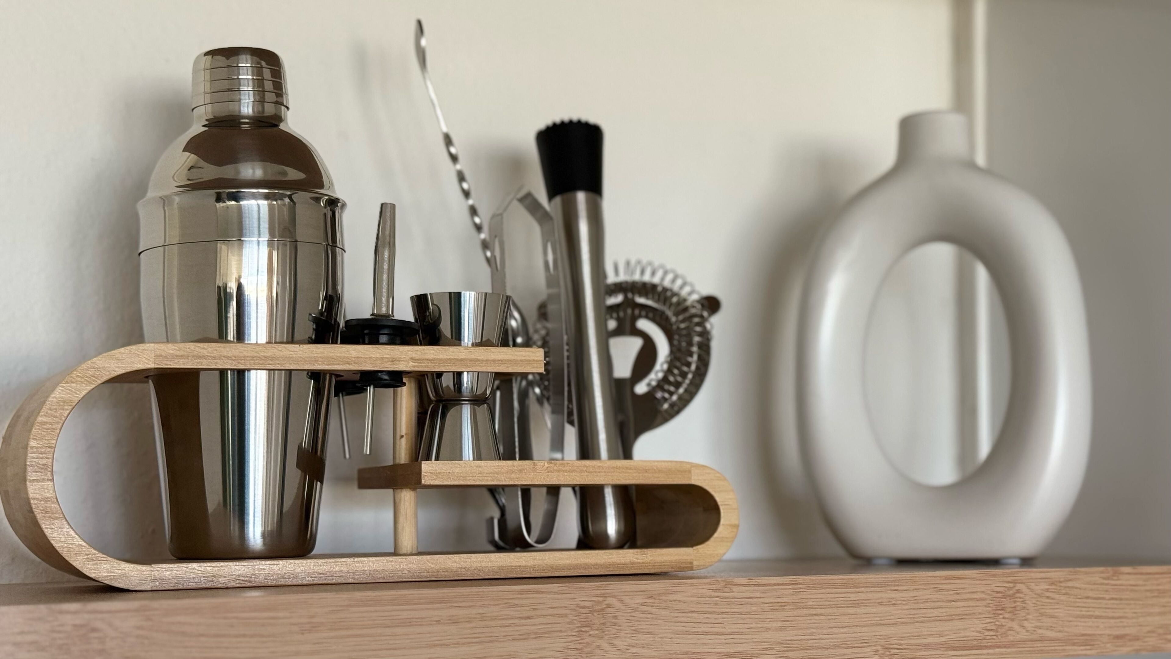 Un vassoio di legno con uno shaker per cocktail, una frusta, un aprisottoli e un cavatappi.