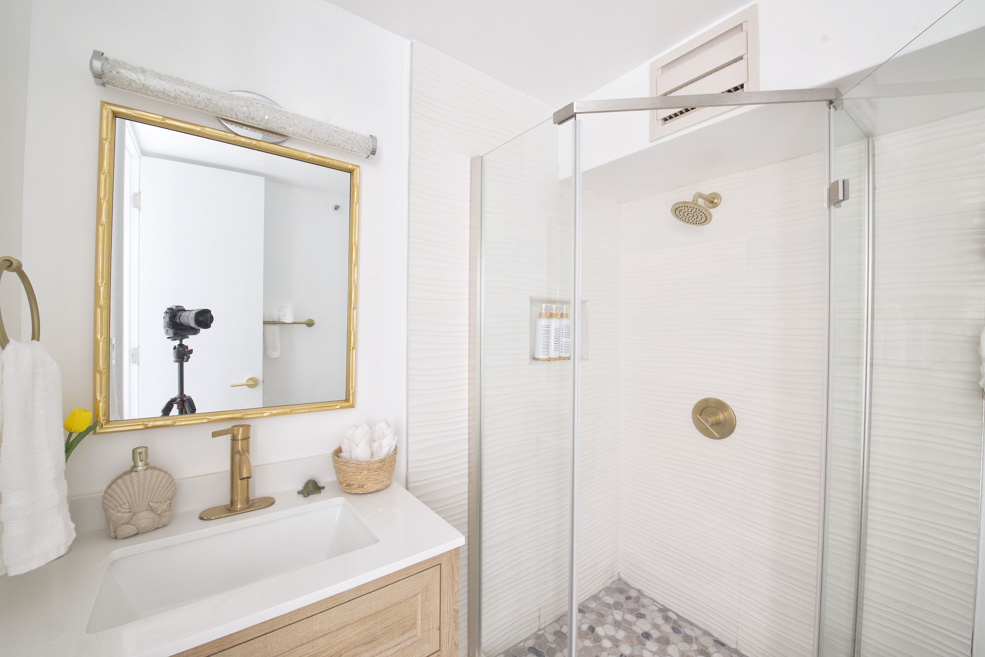 A bathroom with a white sink, gold-framed mirror, and a glass-enclosed shower.